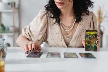 Wall Mural - Cropped view of soothsayer holding blurred tarot cards near table.