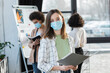 © LIGHTFIELD STUDIOS - Young businesswoman in medical mask holding paper folder near blurred multiethnic colleagues.