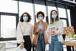 © LIGHTFIELD STUDIOS - Interracial businesswomen in medical masks holding devices and papers in office.
