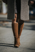 Vertical shot of woman wearing fashionable brown suede knee-high boots outdoors