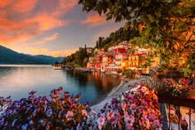 Village Of Varenna On Lake Como At Sunset With Illuminated Houses And Colorful Flowers In The Foreground