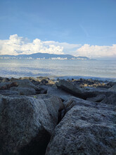 Rocks On The Beach At Robina Park With Mountains On The Horizon Against Blue Sky. Penang, Malaysia