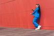 © Dani D.G - Cheerful black woman listening to music near red wall