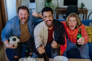 Wall Mural - Happy German football fans friends watching football at home and eating popcorn.