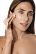 Leinwandbild Motiv Close up shot of middle aged beautiful woman applies anti aging cream on face undergoes beauty treatments cares about skin poses against beige background. Wrinkled female model with cosmetic product