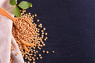 Soya beans with wooden spoon and burlap on the black surface of the slate stone, top view, closeup with space for text