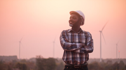 African engineer man stands with front the wind turbines generating electricity power station in sunset. .Concept of sustainability development by alternative energy