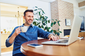 Wall Mural - Relaxed casual man working on laptop drinking coffee at home