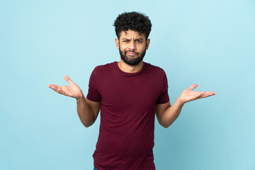 Young Moroccan man isolated on blue background having doubts while raising hands