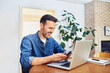 © baranq - Smiling mid adult man using smart phone and laptop at home while working remotely