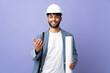 © luismolinero - Young architect Moroccan man with helmet and holding blueprints over isolated background inviting to come with hand. Happy that you came