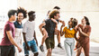 Multiracial young people having fun together walking on city street - Happy group of friends socializing outside - Friendship concept with guys and girls smiling and joking in summer day out