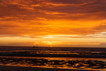 Wall Mural - Beautiful sunset with dramatic moody cloudy sky above the ocean of North Sea and silhouette of a ship, De Haan, Belgium.