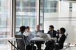 © fizkes - Serious adult female business leader instructing diverse team on brainstorming session at meeting table. Group of coworkers, employees discussing paper marketing reports, project analytics