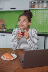Wall Mural - portrait of dreamy happy female holding cup of tea sitting in kitchen at table indoors