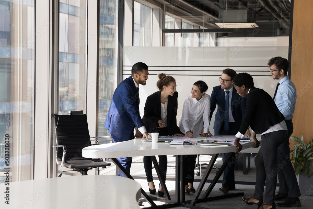 Diverse group of happy employees analyzing reports together, standing ...