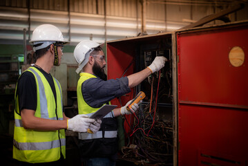 Wall Mural - Electrician latin mixed-race and asian engineer in safety uniforms Inspecting and maintaining the machine's electrical control cabinet in heavy industrial manufacturer factory.