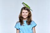 Fototapeta Panele - Child girl with pet green quaker parrot looking at camera on light studio background