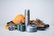 hiking equipment. trekking boots, camera, thermos, clothing, cups on grey desk.