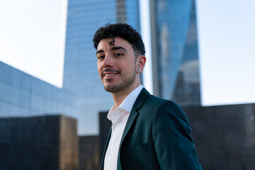 Medium close up. Portrait of Handsome young businessman standing outside the office and smiling happily On the background of city building
