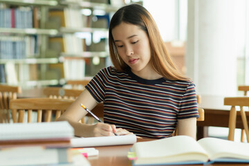 Canvas Print - Female asian student studying and reading book in library