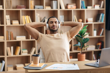 Wall Mural - Man relaxing at workplace and listening to favorite music in wireless headphones, enjoying song with closed eyes