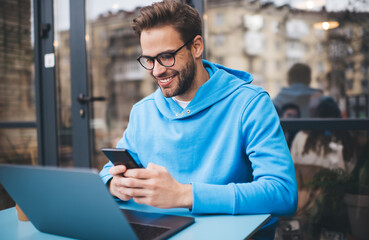 smiling male student with modern laptop computer using cellular application for network chatting in 
