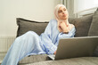 © Svitlana - Muslim woman sitting on couch with laptop at home
