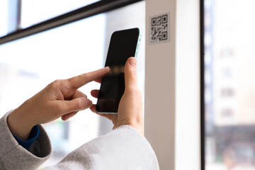 Woman scanning QR code with her smartphone in public transport, closeup