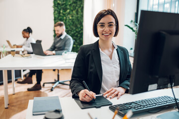 Wall Mural - Female graphic designer working on a drawing tablet in open space office