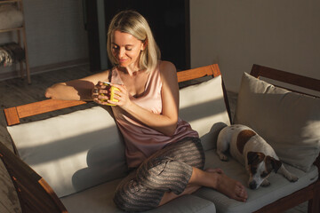 Wall Mural - Adult woman sitting on the sofa at home and having a cup of coffee