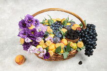 Large Basket With Ripe Fruits And Purple Flowers On A Gray Background