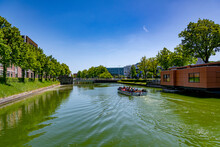 A Tourist Boat Full Of People Sailing Down The Water Canal With Rows Of Green Trees On A Summer Sunny Day