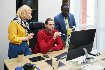 Wall Mural - Group of designers looking at computer monitor and discussing presentation online during teamwork at office