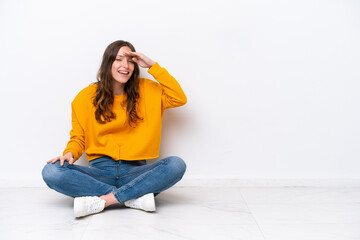 Sticker - Young caucasian woman sitting on the floor isolated on white wall looking far away with hand to look something