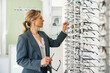 © Friends Stock - Focused Middle-aged woman in jacket trying to choose glasses in an optics store