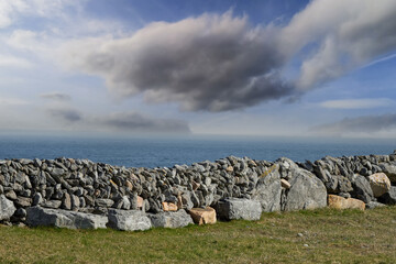 Traditional stone fences or walls in foreground, cloudy sky and blue ocean in background. Inishmaan, Aran Island, county Galway, Ireland. Beautiful Irish nature landscape.