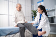 Asian woman physician doing legs raise exercise for senior man patient. 