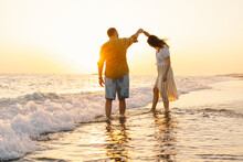 Young Romantic Couple Dancing Turning Around By Sea. Seascape At Sunset With Beautiful Sky. Romantic Couple On The Beach At Golden Sunset. Lover Couple Having Fun On Beach.