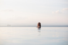 A Young Woman Relaxing In Infinity Swimming Pool With A Beautiful Island And Sea View