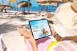 Leinwandbild Motiv Woman relaxing on beach and reading travel blog on tablet computer