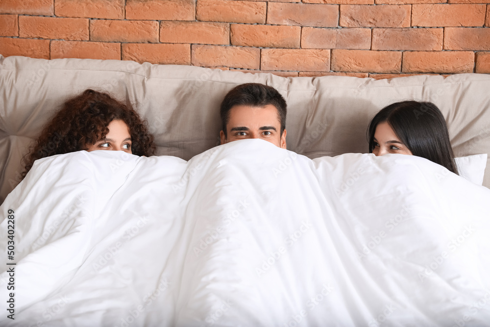 Man with two beautiful women in bed. Polyamory concept