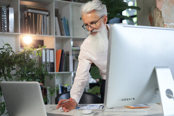 Sticker - Senior businessman with a stylish beard working on laptop computer at his office desk.