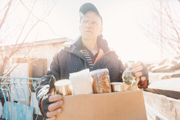 Wall Mural - Concept humanitarian aid community charity donations center with sunlight. Homeless refugee is holding box food