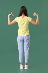 Wall Mural - Pretty young woman in stylish t-shirt on green background, back view