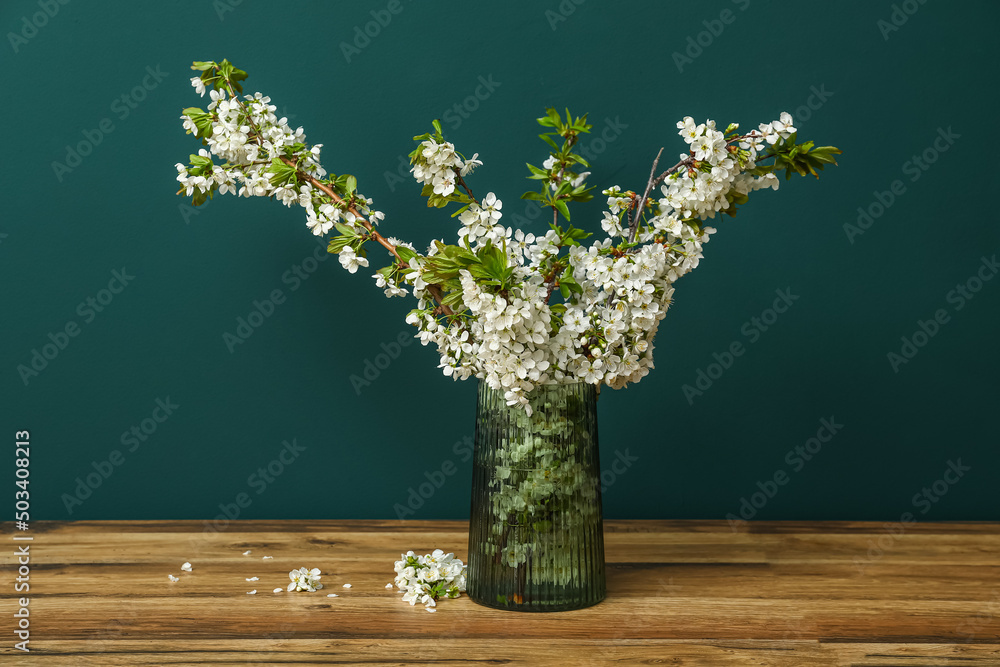 Vase with beautiful blooming tree branches on wooden table near green wall