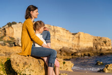 Happy Woman And Daughter Sitting On Rock At Beach