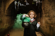 Cute Girl Holding Cauldron With Witches Brew Wearing Witch Costume In Spooky Tunnel