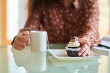 Hands Of Woman Holding Muffin And Coffee Cup At Table