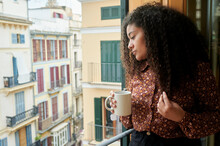 Young Woman Holding Coffee Cup Looking Through Window At Home